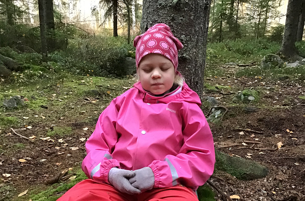 Tyttö istuu metsässä ja nojaa puun runkoon.